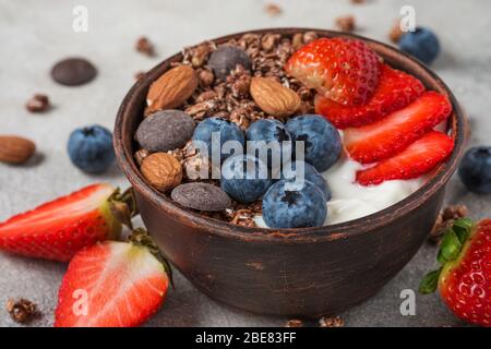 bowl of oat chocolate granola with yogurt, fresh blueberries, strawberries and nuts on gray background for healthy breakfast. close up Stock Photo