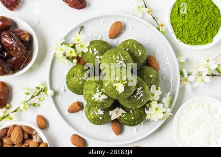 Homemade raw energy balls made of green matcha tea, dates and nuts with spring flowers. Top view. Healthy vegan dessert food on white background. Food Stock Photo