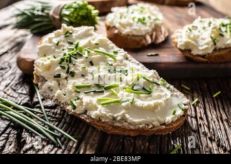 Close-up of bread slice with traditional Slovak bryndza spread made of sheep cheese with freshly cut chives placed on rustic wood. Stock Photo