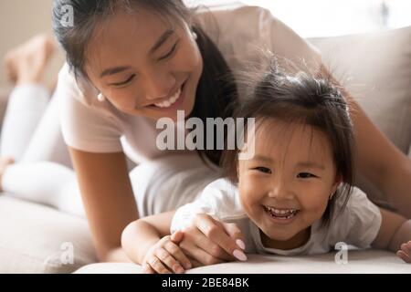 Asian little girl spending active funny time with mother indoors Stock Photo