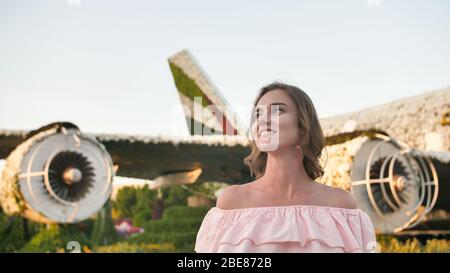 A girl admires in a city park on the background of an airplane of flowers. Stock Photo