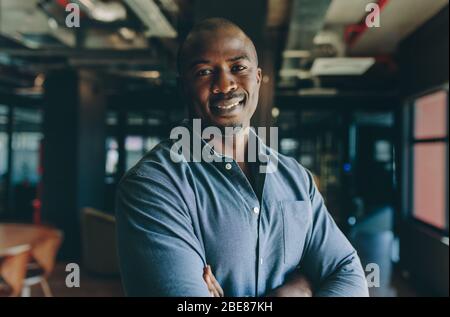 Confident businessman standing in office. African man standing with his arms crossed looking at camera and smiling.