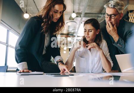 Businesswoman discussing new strategies with her team sitting around a table. Group of business people having a meeting on new project in office. Stock Photo