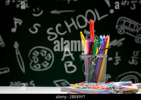 School background with stationery accessories. Books, globe, pencils and various office supplies lying on the desk on a green blackboard background Stock Photo