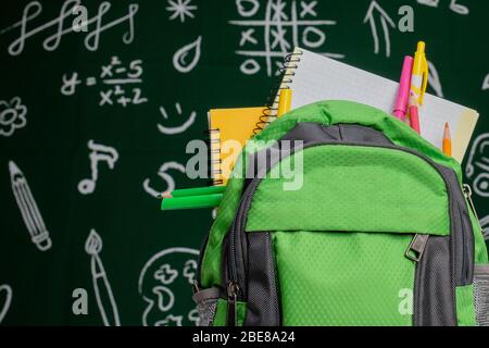 Education concept - green backpack, notebooks and school supplies on the background of the blackboard Stock Photo