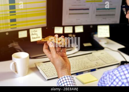 Busy business man eating healthy avocado toast breakfast in a hurry while working on computer Stock Photo