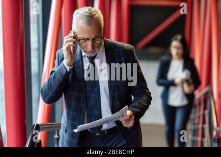 businessman in suit talking on smartphone and reading newspaper Stock Photo