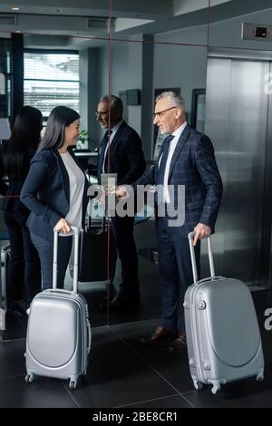 smiling businessman and asian businesswoman with travel bags pushing button of elevator Stock Photo
