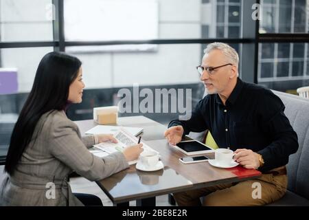 smiling businessman and businesswoman sitting at table and talking in cafe Stock Photo