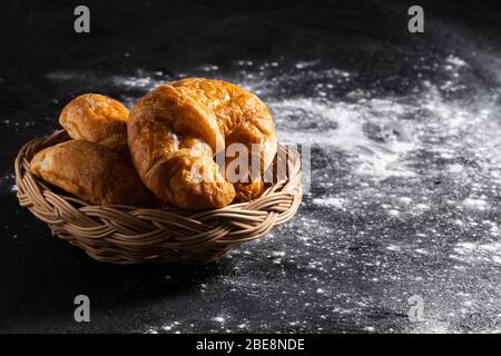 Croissants in a wicker basket placed on a black floor which makes pastry dough. Stock Photo