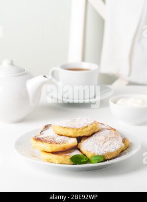 Fried cheese cakes, sweet cheese pancakes on white plate on white background. Home tea party Stock Photo