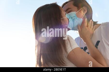 Young man and woman kissing with surgical face masks on, quarantine, Covid-19 protection. Love during coronavirus pandemic.