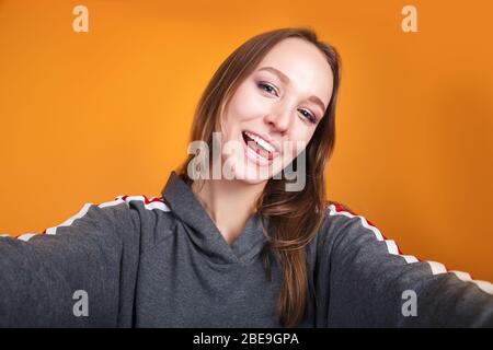 Close-up of young funny woman taking selfie on yellow background