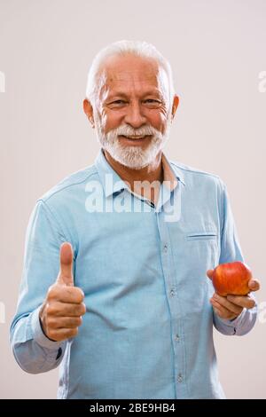 Portrait of cheerful senior man who is holding apple and smiling. Stock Photo