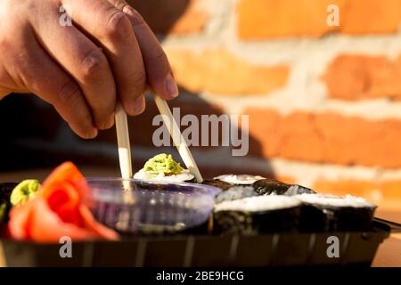 hand with sticks takes a roll from a box with sushi on the street close-up. Stock Photo