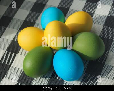 Colorful Easter eggs lie on a checkered tablecloth. Yellow, blue, green eggs. Still-life. Stock Photo