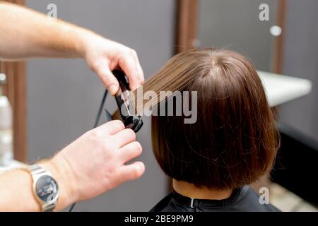 Hairdresser straightens hair of woman with hair straightener tool in hair salon. Stock Photo