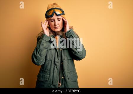 Middle age beautiful blonde skier woman wearing snow sportwear and ski goggles with hand on headache because stress. Suffering migraine. Stock Photo