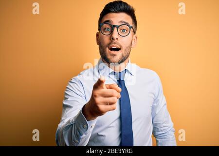 Young handsome businessman wearing tie and glasses standing over yellow background pointing displeased and frustrated to the camera, angry and furious Stock Photo