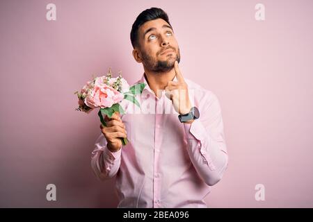Young romatic man holding bouquet of spring flowers over pink isolatd ...
