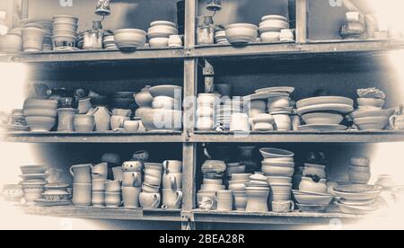 Old vintage style photo. Many different pottery standing on the shelves in a pottery workshop. Low light Stock Photo