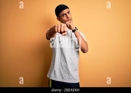 Handsome african american sportsman doing sport wearing sportswear over yellow background Punching fist to fight, aggressive and angry attack, threat Stock Photo