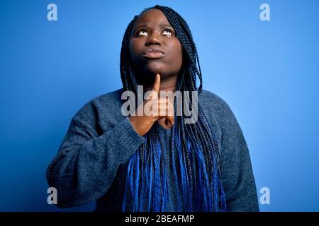 African american plus size woman with braids wearing casual sweater over blue background Thinking concentrated about doubt with finger on chin and loo Stock Photo