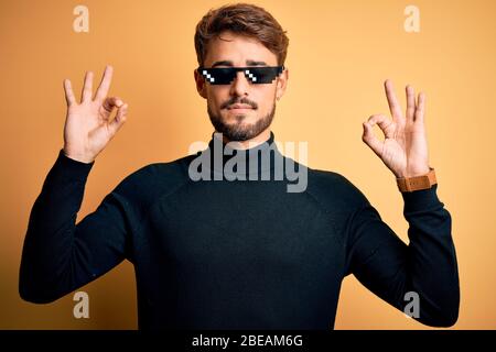 Young man wearing thug life fanny sunglasses standing over isolated yellow background relax and smiling with eyes closed doing meditation gesture with Stock Photo