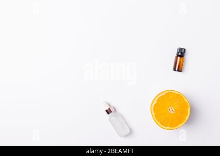 Fresh orange fruit next to cosmetic serum with vitamin C and bottle of essential oil, flat lay composition on white background. Stock Photo
