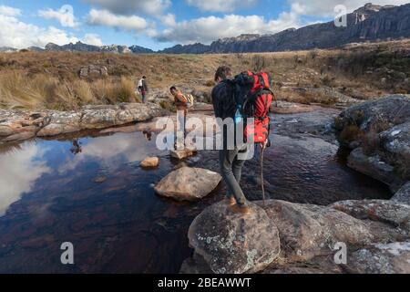 Andringitra, Madagascar : Hikers with backpacks cross river in national park Stock Photo