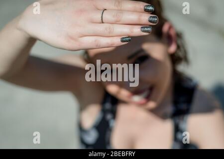Sunlight hand protection. Young woman covering with hand's shadow the eyes to avoid sunlight. Focus on the hand. Stock Photo