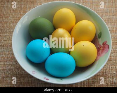 Colorful Easter eggs lie in a white porcelain plate. Blue, green, yellow, Golden eggs. Still-life. Stock Photo