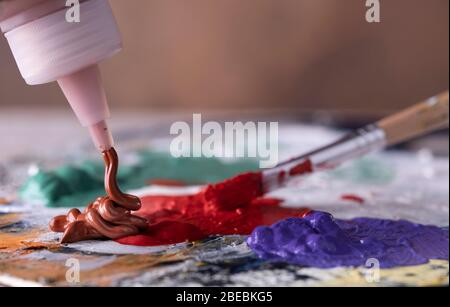 Creative artist using paintbrush to mix green and red oil paint on colorful palette. Stock Photo