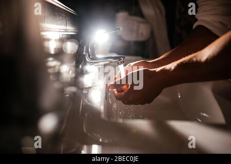 closeup of a young caucasian man washing his hands in the sink in bathroom Stock Photo