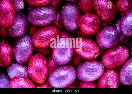 A top down close up portrait of a bunch of colorful chocolate easter eggs wrapped in tin foil lying on top of each other. Ready to be eaten. They are Stock Photo