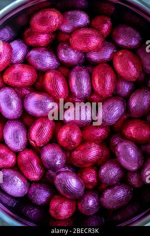 A top down close up portrait of a bunch of colorful chocolate easter eggs wrapped in tin foil lying on top of each other lying in a metal pot. Ready t Stock Photo