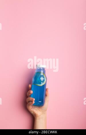 Blue detox water with lemon slice in woman hand on pink