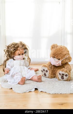 teddybear and a doll with a homemade covid 19 protection mask sitting on the floor Stock Photo