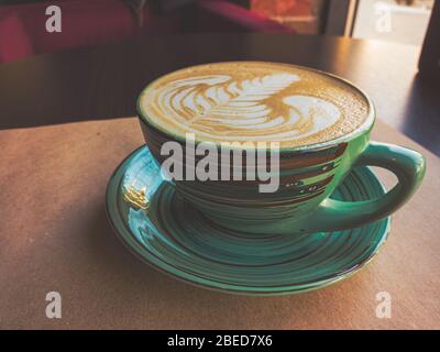A large cappuccino cup of green color stands on a table covered with Kraft paper. Toning imitates an old film photo. Stock Photo