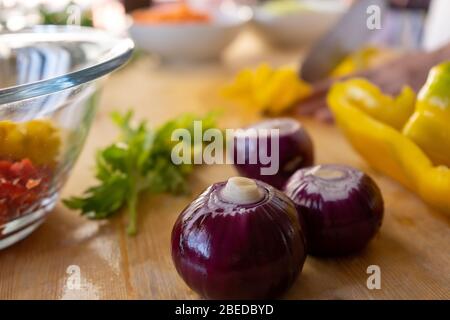 Moments of daily life in the Mediterranean cookery: low angle view of three onions on foreground while womans cutting vegetable in background on light Stock Photo