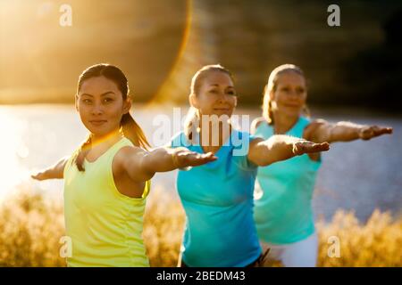 Three women practicing yoga next to a river Stock Photo