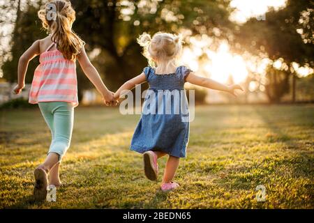 Two young girls running hand in hand through a park Stock Photo