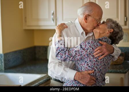 Senior couple sharing a kiss in their kitchen Stock Photo