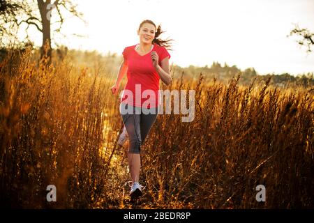Young woman jogging through tall grass on a trail in the late afternoon sunlight Stock Photo