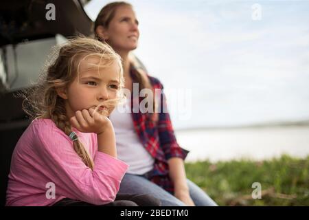 Young girl sitting with her mother on the back of a car looking out at a scenic view Stock Photo
