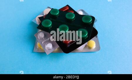 Packs of pills of various shapes and colors are stacked on a blue background. Capsules are packaged in blister packs. Different medicines. Drug treatm Stock Photo