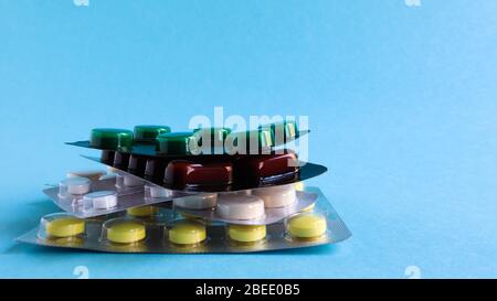 Packs of pills of various shapes and colors are stacked on a blue background. Capsules are packaged in blister packs. Different medicines. Drug treatm Stock Photo