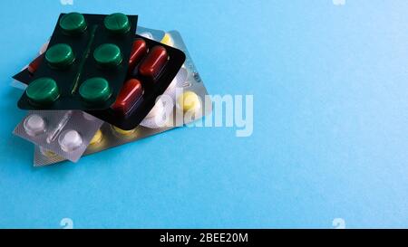 Packs of pills of various shapes and colors are stacked on a blue background. Capsules are packaged in blister packs. Different medicines. Drug treatm Stock Photo