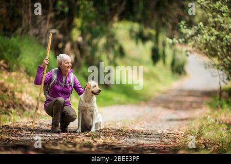 Portrait of a cheerful mature woman taking a break from hiking in the forest with her dog Stock Photo