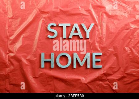 the words stay home laid with silver metal letters on crumpled red plastic background in flat lay perspective, directly above composition Stock Photo
